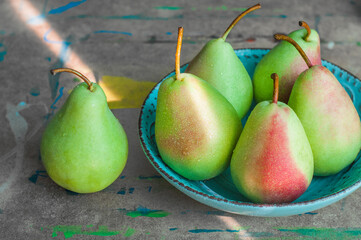 Green pears with red sides lying on a turquoise plate on the table in watercolor paint.