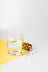 Glass of water and pills from a jar on white and yellow backgrounds