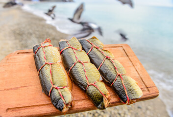 Smoked fish on a wooden board against the background of the sea and a flock of flying birds