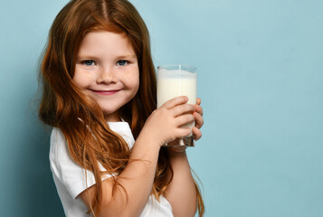 Cute red hair girl child kid drinking milk or kefir yogurt joyfully smiling on light blue...