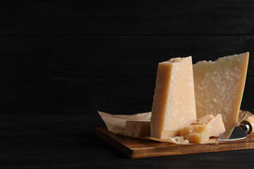 Parmesan cheese with board and knife on black wooden table. Space for text