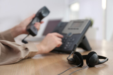 Obraz na płótnie Canvas Woman using desktop telephone in office, focus on headset. Hotline service