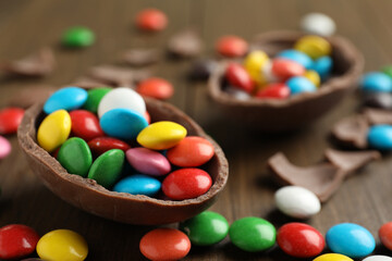 Fototapeta na wymiar Broken chocolate egg and colorful candies on wooden table, closeup