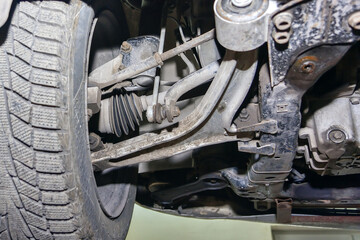 The wheel, suspension and chassis of a car standing on a car lift close-up.