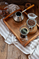 Coffee still life. Grains of coffee in a glass jar, a turk for brewing coffee on a wooden tray. Breakfast on the table