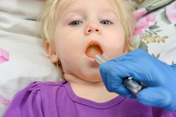 The doctor examines the oral cavity with a medical flashlight in a sick child.