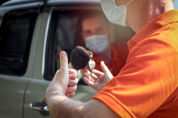 Car service technician giving thumb up while taking the key from another man in car, auto mechanic driving customer car to automobile service center for checking and repairing
