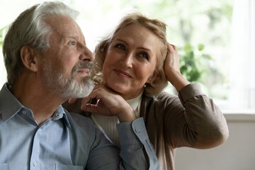 Fototapeta premium Close up dreamy mature spouses dreaming together, visualizing future, looking to aside, happy satisfied elderly grey haired man and woman lost in thoughts, enjoying leisure time at home
