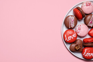 Assorted Valentines Day macarons with Love written on them on a pastel pink background on a white plate with copy space and room for text with a right side composition