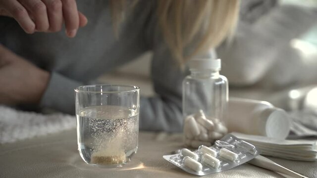Chora kobieta wrzuca do szklanki z wodą tabletkę musującą, 
