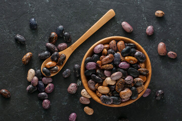 Dry beans in a wooden bowl on a black background, top view.