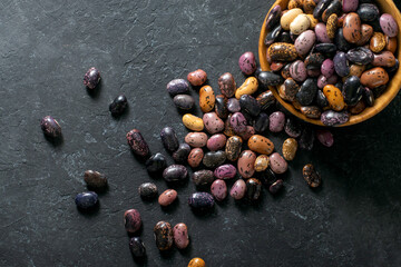 Beans spilling out from a wooden bowl on a black background, top view.