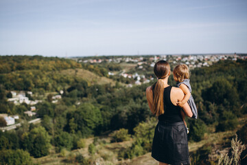 Mom with daughter in her arms on the mountain looking at the city. Rear view