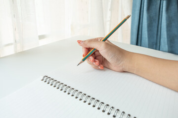 Close up female's hand writing on a notebook paper with pencil