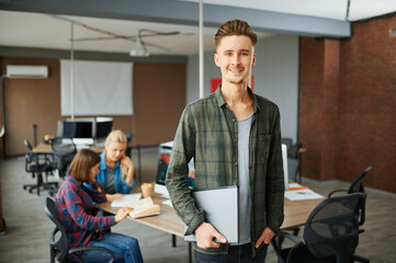 Smiling male IT specialist holds laptop in office
