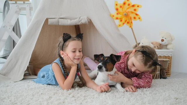 Little girls with fox terrier lying in wigwam on kids room floor