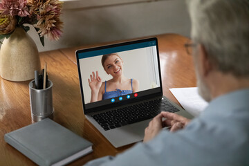 View from shoulder mature man making video call to relatives, using computer, watching webinar, learning language in internet, smiling young woman on laptop screen waving hand, chatting online