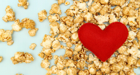 Red soft felt heart on a pile of popcorn on a blue background. Banner. Concept: fast food for Valentine's Day. The view from the top