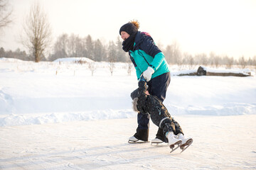 Fototapeta na wymiar young mother teaching her little son ice skating at outdoor skating rink. Family enjoy winter on ice-rink outdoors