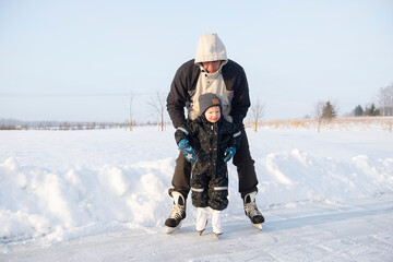 Fototapeta na wymiar Grandfather teaching her little grandson ice skating at outdoor skating rink.