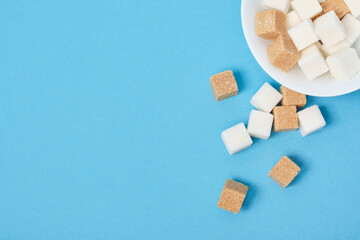 cubes of brown and white sugar sprinkled from a white bowl on a blue background