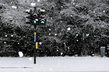 Green traffic light for pedestrians on snowy street during snowfall in England, United Kingdom (UK)