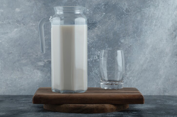 Jug of fresh milk and glass of water on wooden board