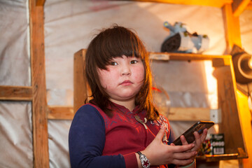 A young girl, in the national winter clothes of the northern inhabitants of the tundra, takes a selfie on a smartphone