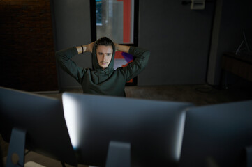 Male internet hacker in hood leisures at monitors