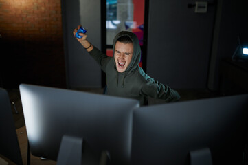 Mad male hacker in hood sitting at screens, back view