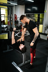 Fototapeta na wymiar Men working out, personal trainer helping and assisting client in the gym.