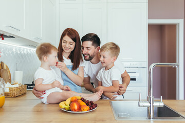 Happy family, husband woman and two children boys, having breakfast at home in the kitchen, and spending happily together