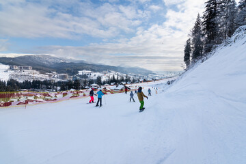 Panorama of ski resort, slope, people on the ski lift, skiers on the piste among white snow pine trees