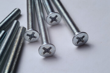 metal screws with a cross-head screwdriver slot lie on a light background. close-up.
