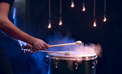 The drummer plays with mallets on floor tom in dark room.