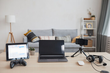 Background image of gaming station with laptop, gamepad and video streaming equipment in minimal home interior, copy space