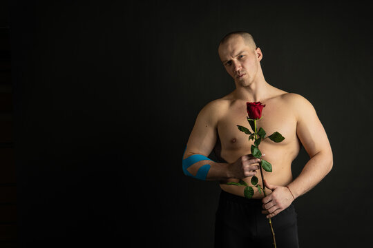 Athletic man holding a red rose, naked for the day of velentin pumped up, on his arm a teip of a bodybuilder romantic. lover guy LGBT. In the studio on a black background Smiling with a lovely smile