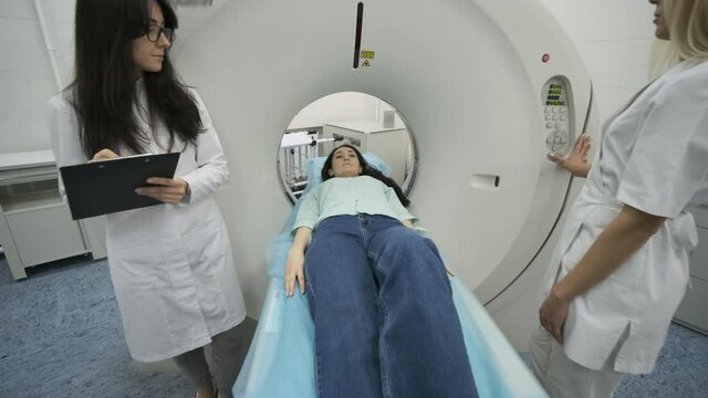 Female patient is undergoing CT or MRI scan under supervision of two qualified radiologists in modern medical clinic. Patient lying on a CT or MRI scan table