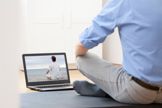 Businessman doing yoga or meditation exercise in front of laptop with man doing yoga on a beach