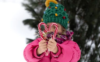 Warmly dressed little girl holding candy canes close up.