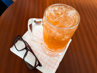 High angle shot of a Malt beer with ice cubes, a napkin and eyeglasses on the table.
