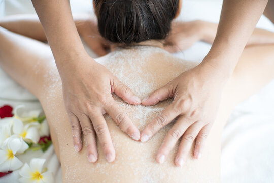 Female Spa Staff Doing Salt Spa For Asian Women. Young Asian Woman Having Exfoliation Treatment With Body Scrub In Spa Salon.