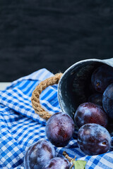 Small bucket of garden plums on a dark background with tablecloth