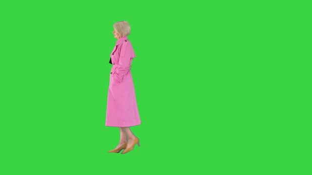 Rich senior woman in pink trench coat walking by on a Green Screen, Chroma Key.
