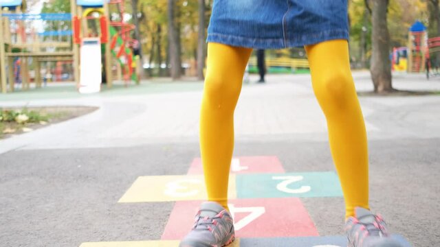 Legs of little girl in bright tights jumping over numbers on asphalt