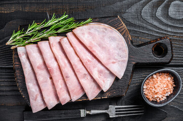 Sliced prosciutto ham on wooden cutting board. Black wooden background. Top view