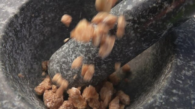 Pieces of the sweet brown sugar are falling into the grey stone mortar in slow motion