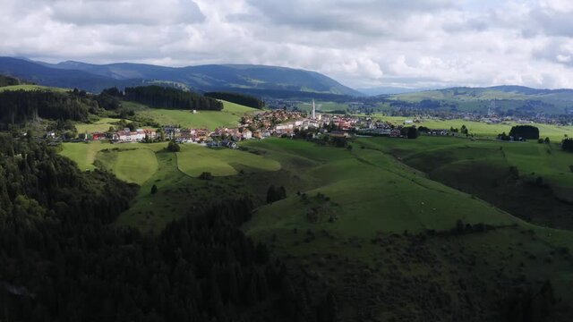 Aerial wide shot of Camporovere Village surrounded by beautiful colorful landscape during sunny and cloudy day in Italy. Rural and scenic area with forest trees and mountains in background.
