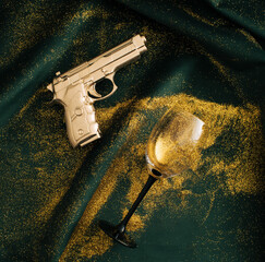 Gold glitter with golden gun and wine glass on green fabric. Flat lay