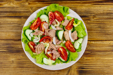 Tasty tuna salad with lettuce and fresh vegetables on wooden table. Top view